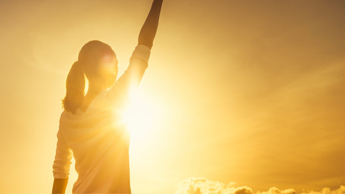 Silhouette of a woman holding her hand in the air demonstrating courage with a bright sun in the background. Tips to push yourself out of your comfort zone, Jewmei blog