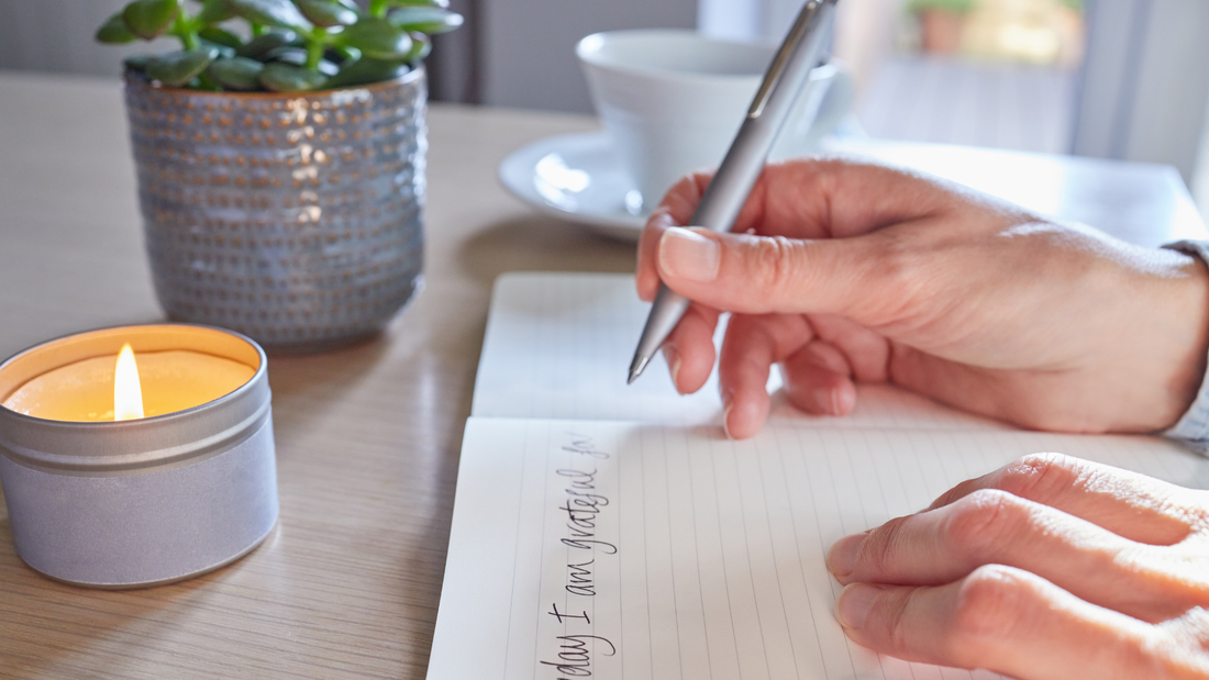 Image of a woman holding a pen writing in a notebook at a table wearing gold jewelry from Jewmei