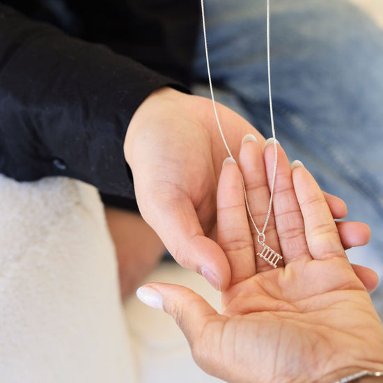 Someone receiving One Step at a Time minimalist silver necklace from Jewmei in their hands.