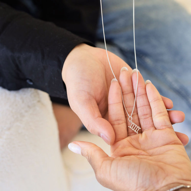 Someone receiving One Step at a Time minimalist silver necklace from Jewmei in their hands.