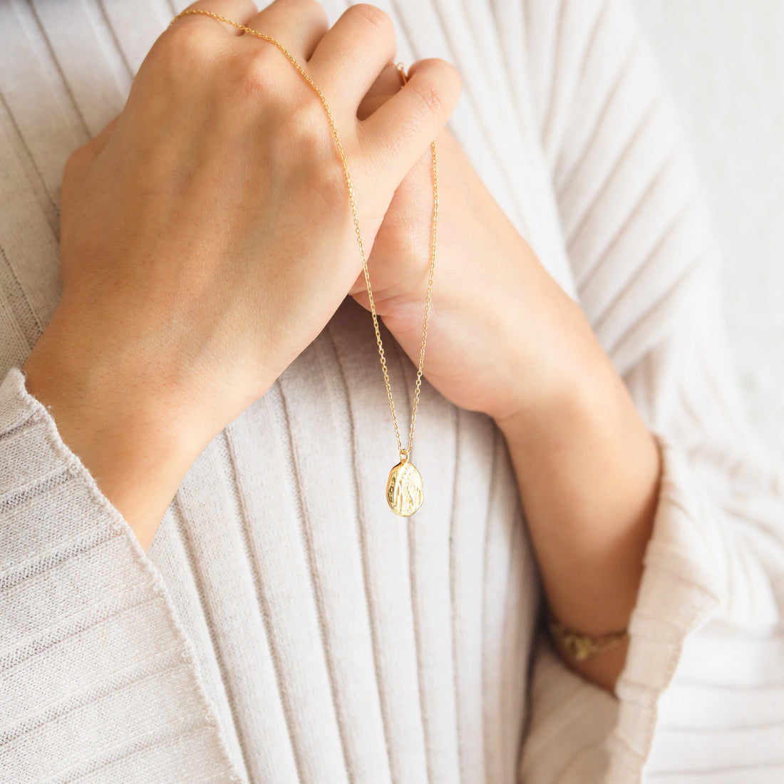 Image of a woman wearing a white cardigan holding a gold necklace from Jewmei, online jewelry store in Canada