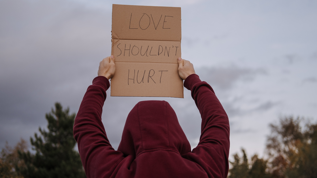 Woman in red hoodie, holding up a cardboard sign that reads "Love Shouldn't Hurt" to Motivate, Inspire and encourage